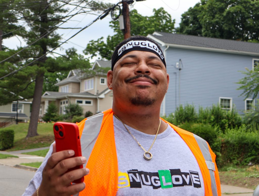 A smiling man in a neighborhood holding a cellphone
